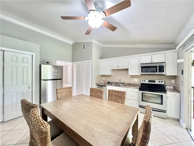 Kitchen featuring stainless steel appliances, crown molding, backsplash, and white cabinetry