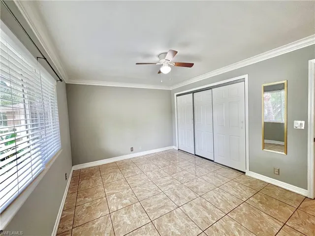 Unfurnished bedroom featuring ceiling fan, ornamental molding, light tile flooring, and multiple windows