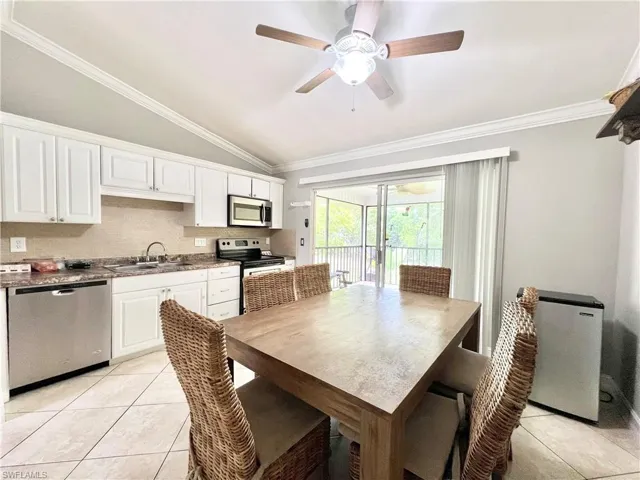 Tiled dining space featuring ceiling fan, sink, crown molding, and lofted ceiling