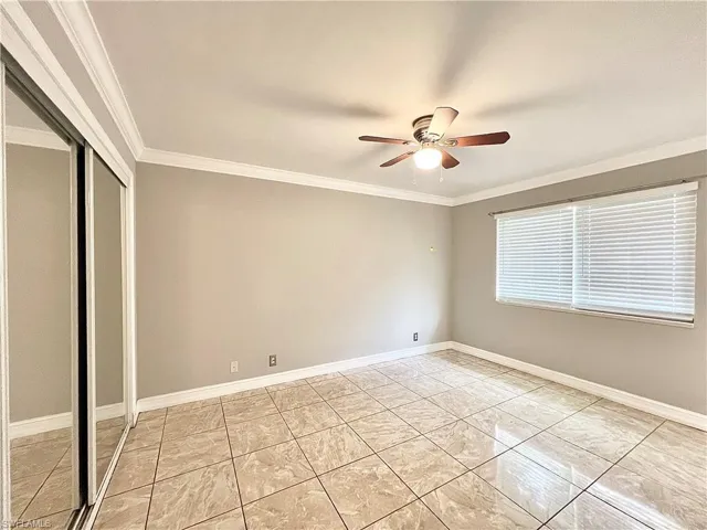 Unfurnished bedroom with ornamental molding, light tile flooring, ceiling fan, and a closet