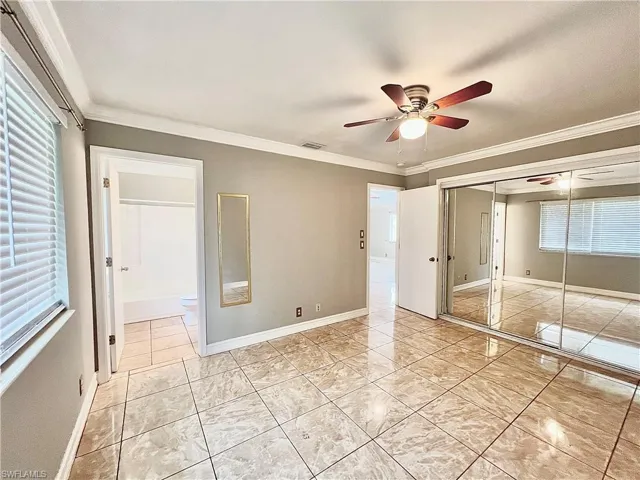 Unfurnished bedroom featuring ornamental molding, a closet, ensuite bathroom, ceiling fan, and light tile floors