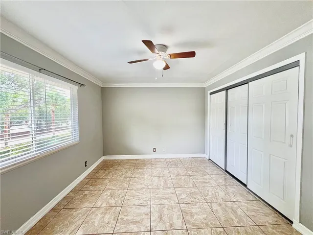 Unfurnished bedroom featuring ceiling fan, ornamental molding, and light tile flooring