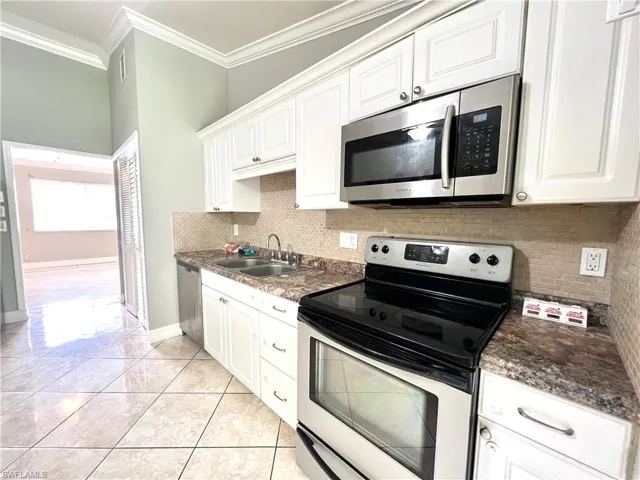 Kitchen featuring white cabinetry, ornamental molding, appliances with stainless steel finishes, sink, and tasteful backsplash
