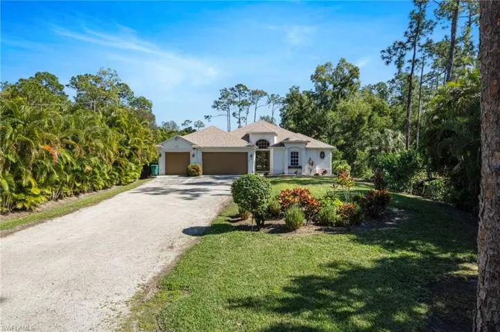 View of front of house featuring a front yard, driveway, a garage, and view of wooded area