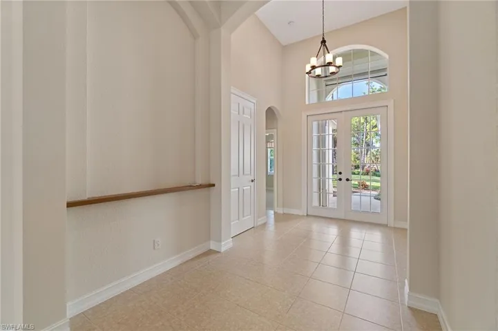Foyer entrance with french doors, arched walkways, a towering ceiling, light tile patterned floors, and a chandelier