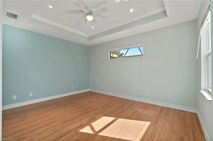 Bedroom with a raised ceiling, light wood floors, crown molding, recessed lighting, and a ceiling fan.