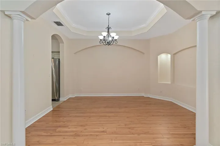 Dining area featuring decorative columns, arched walkways, light wood-type flooring, crown molding, and a chandelier