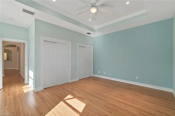 Unfurnished bedroom featuring multiple closets, arched walkways, light wood finished floors, ceiling fan, and a tray ceiling
