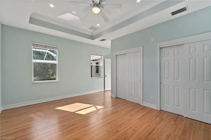 Unfurnished bedroom featuring multiple closets, light wood finished floors, a raised ceiling, ceiling fan, and crown molding