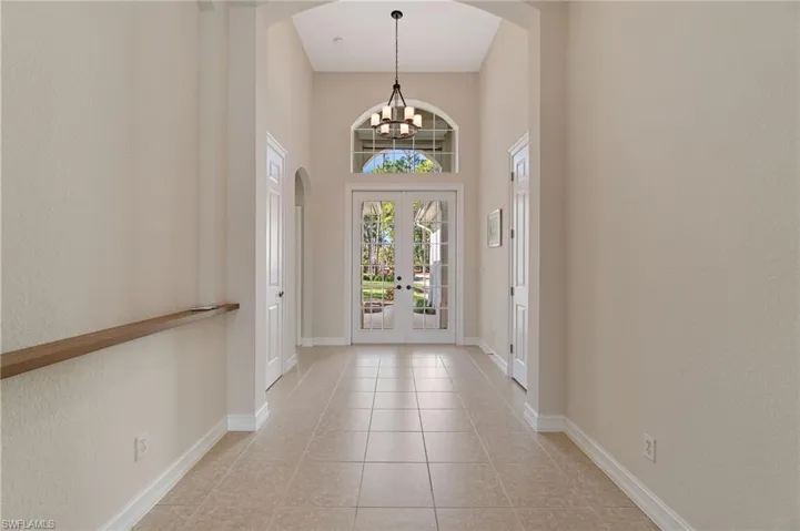 Foyer entrance with arched walkways, french doors, a high ceiling, light tile patterned floors, and a chandelier