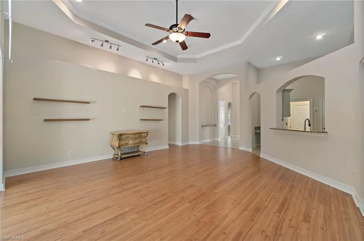 Unfurnished living room with a raised ceiling, light wood-style floors, ornamental molding, a ceiling fan, and arched walkways