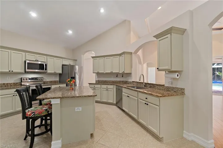 Kitchen featuring arched walkways, natural stone counters, a breakfast bar area, stainless steel appliances, and a kitchen island