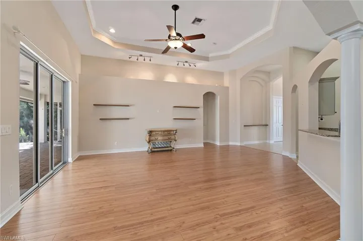 Unfurnished living room featuring light wood-style flooring, ornamental molding, ceiling fan, a tray ceiling, and arched walkways