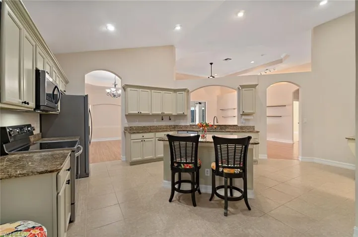 Kitchen with arched walkways, range with electric stovetop, natural stone counters, a breakfast bar, and vaulted ceiling