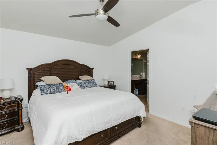 Bedroom with light colored carpet, lofted ceiling, ceiling fan, and connected bathroom