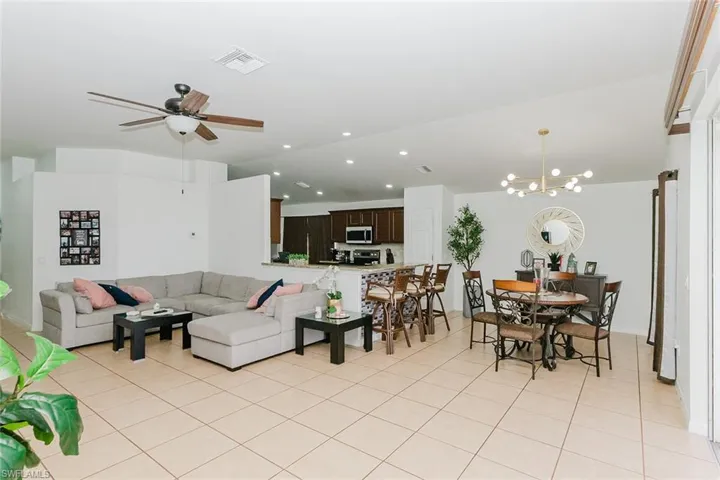 Living area featuring a ceiling fan, suspended lighting, light tile patterned flooring, and vaulted ceiling
