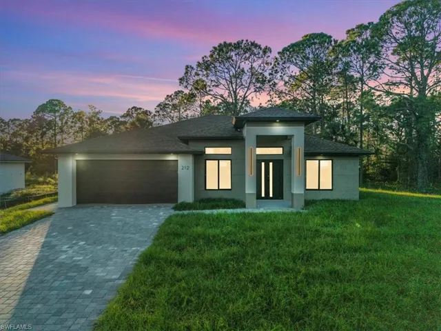 View of front facade featuring a front yard, decorative driveway, stucco siding, a garage, and roof with shingles