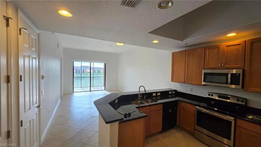 Kitchen featuring appliances with stainless steel finishes, sink, light tile patterned floors, a textured ceiling, and kitchen peninsula