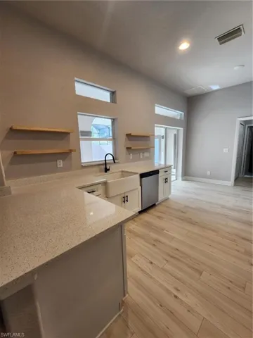 Kitchen featuring light wood-type flooring, white cabinets, light stone counters, sink, and dishwasher