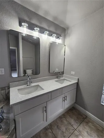 Bathroom with tile floors, dual sinks, oversized vanity, and toilet