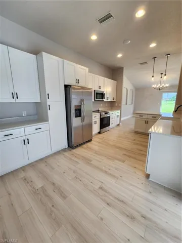 Kitchen featuring stove, stainless steel fridge, light wood-type flooring, white cabinets, and pendant lighting