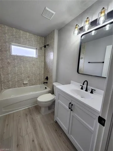 Full bathroom featuring wood-type flooring, tiled shower / bath, a textured ceiling, toilet, and vanity