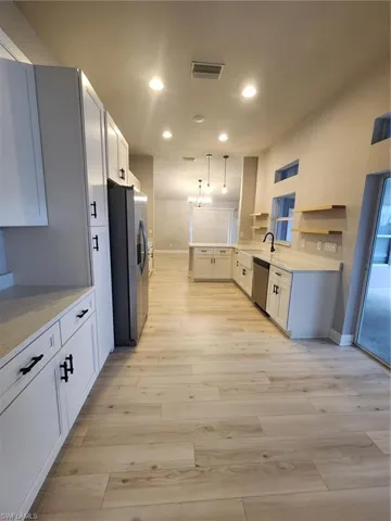 Kitchen with light hardwood / wood-style floors, white cabinets, fridge, pendant lighting, and dishwasher