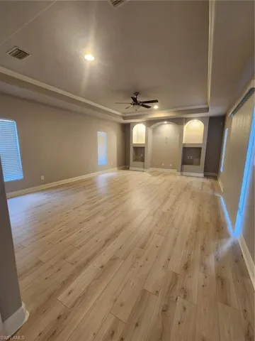 Unfurnished living room with ceiling fan, light hardwood / wood-style flooring, and a raised ceiling