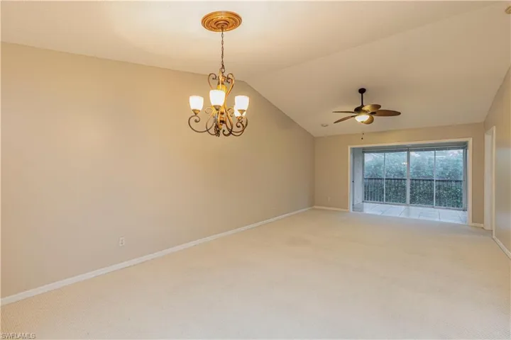 Carpeted spare room with ceiling fan with notable chandelier and lofted ceiling