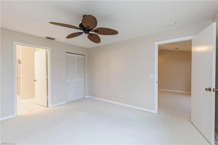 Unfurnished bedroom with a textured ceiling, a closet, ceiling fan, light colored carpet, and ensuite bathroom
