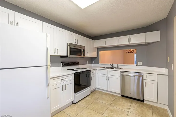 Kitchen with appliances with stainless steel finishes, sink, white cabinetry, light tile patterned flooring, and a textured ceiling