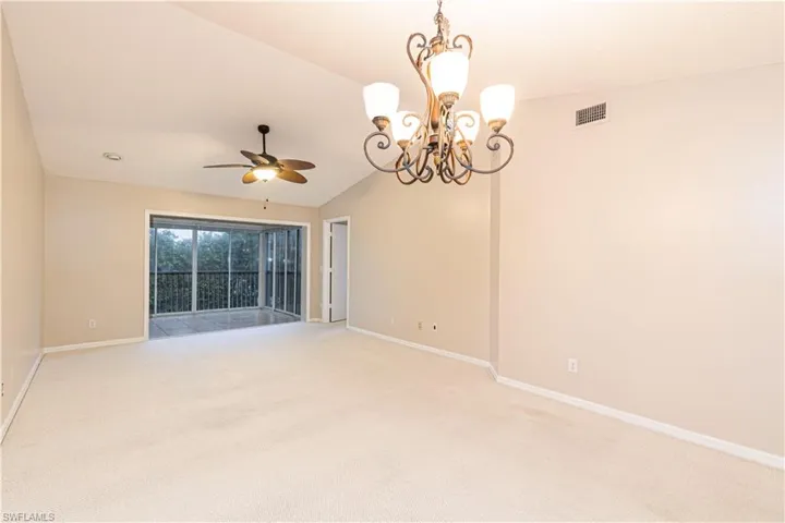 Spare room featuring ceiling fan with notable chandelier, carpet floors, and vaulted ceiling