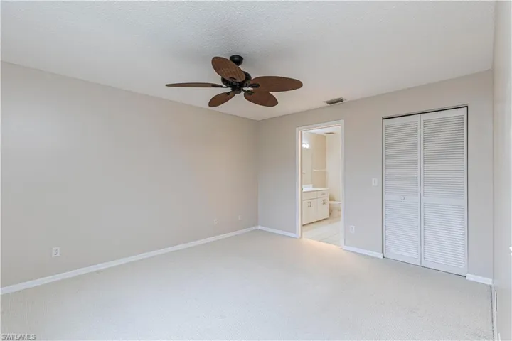 Unfurnished bedroom featuring a textured ceiling, a closet, light colored carpet, ceiling fan, and connected bathroom