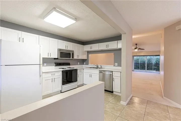 Kitchen with light tile patterned floors, a textured ceiling, white cabinets, and stainless steel appliances