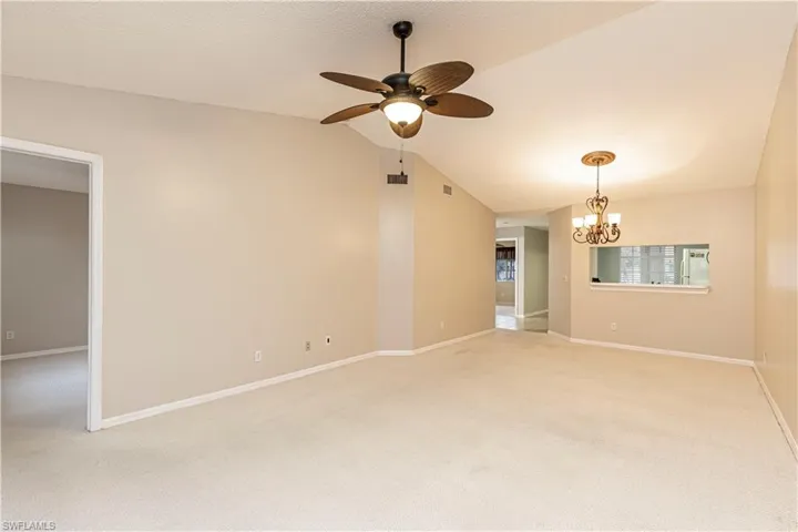 Carpeted spare room featuring ceiling fan with notable chandelier and lofted ceiling