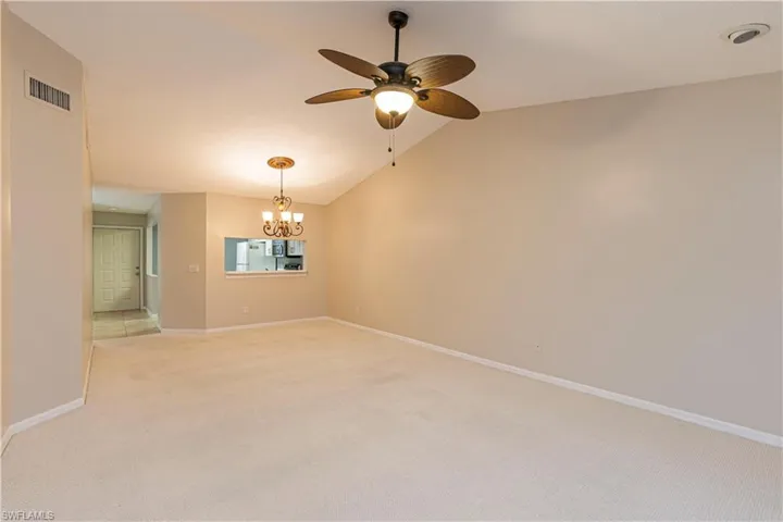 Spare room with light carpet, ceiling fan with notable chandelier, and lofted ceiling