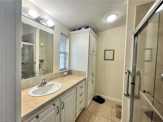 Bathroom with vanity, a textured ceiling, light tile patterned flooring, and a shower stall