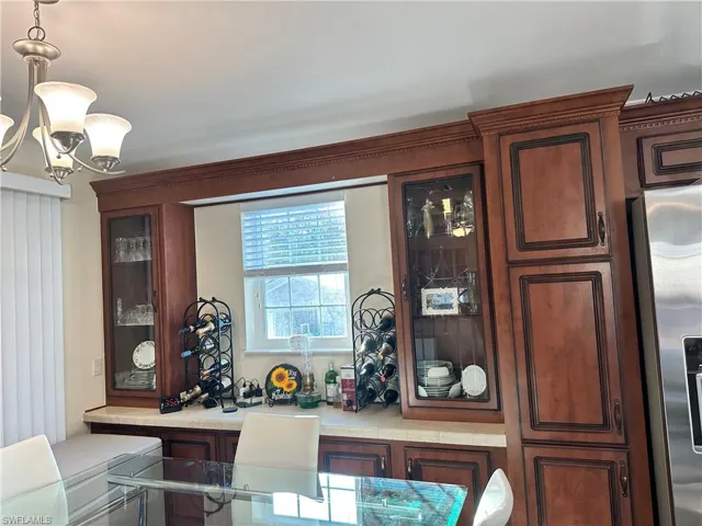 Kitchen with glass insert cabinets, stainless steel fridge, hanging light fixtures, a chandelier, and dark brown cabinets