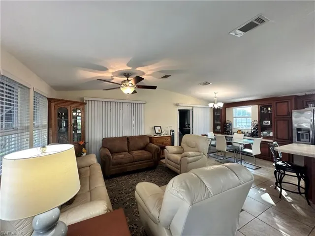 Living area featuring vaulted ceiling, tile patterned flooring, a ceiling fan, and a chandelier