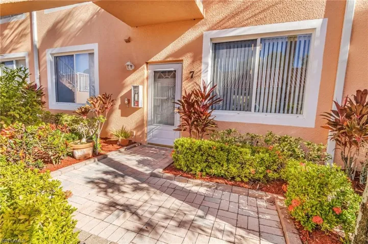 Stucco exterior featuring multiple windows with vertical blinds, a white entry door, and a paver walkway