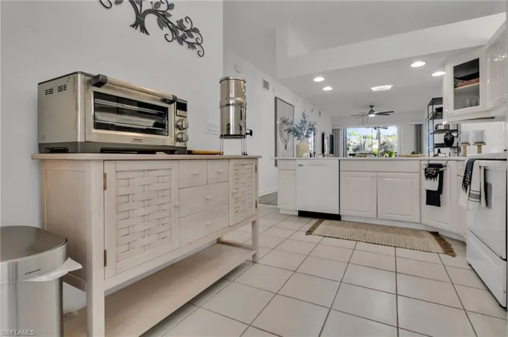 Bright kitchen featuring white cabinetry, white appliances, and light-toned tile flooring