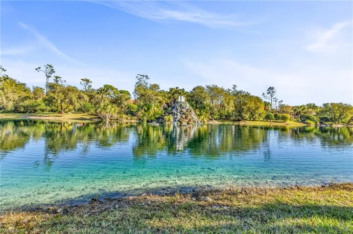 Serene waterfront property featuring clear waters, a rock waterfall, and mature trees lining the distant shore
