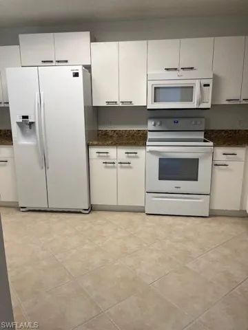 Kitchen with range, light tile patterned floors, refrigerator, and dark stone counters