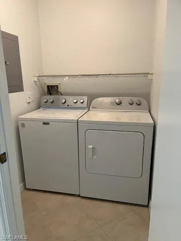 Clothes washing area with washing machine and clothes dryer, electric panel, and light tile patterned floors
