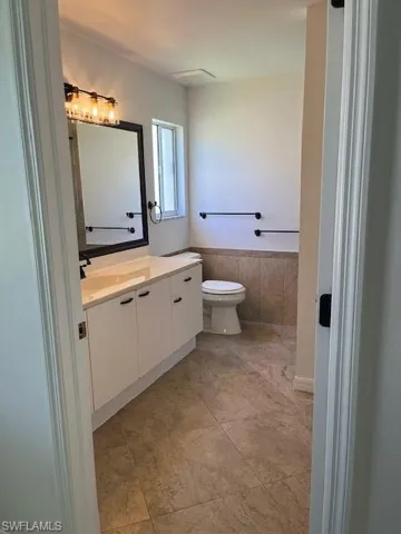 Bathroom with tile walls, toilet, tile patterned floors, and vanity