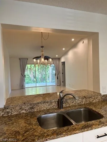 Kitchen featuring dark stone countertops, vaulted ceiling, sink, a chandelier, and decorative light fixtures