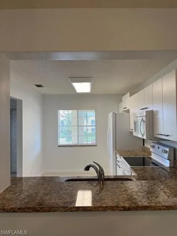 Kitchen featuring dark stone countertops, a textured ceiling, range, and white cabinetry