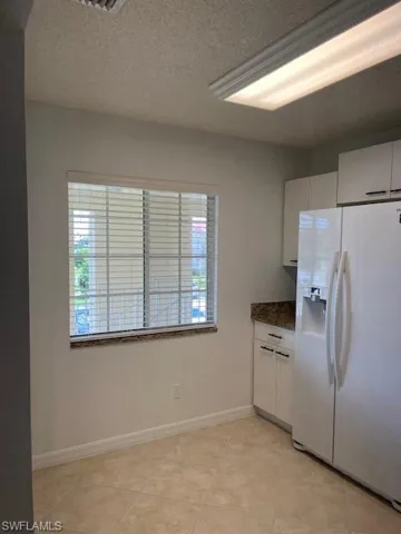 Kitchen with fridge, a textured ceiling, light tile patterned flooring, and white cabinetry