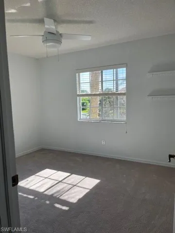 Carpeted empty room featuring ceiling fan and a textured ceiling