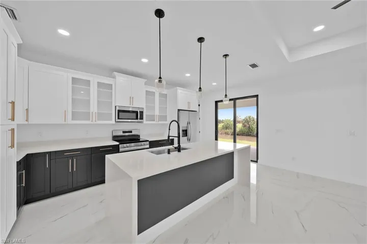Kitchen featuring decorative light fixtures, appliances with stainless steel finishes, a kitchen island with sink, sink, and white cabinetry